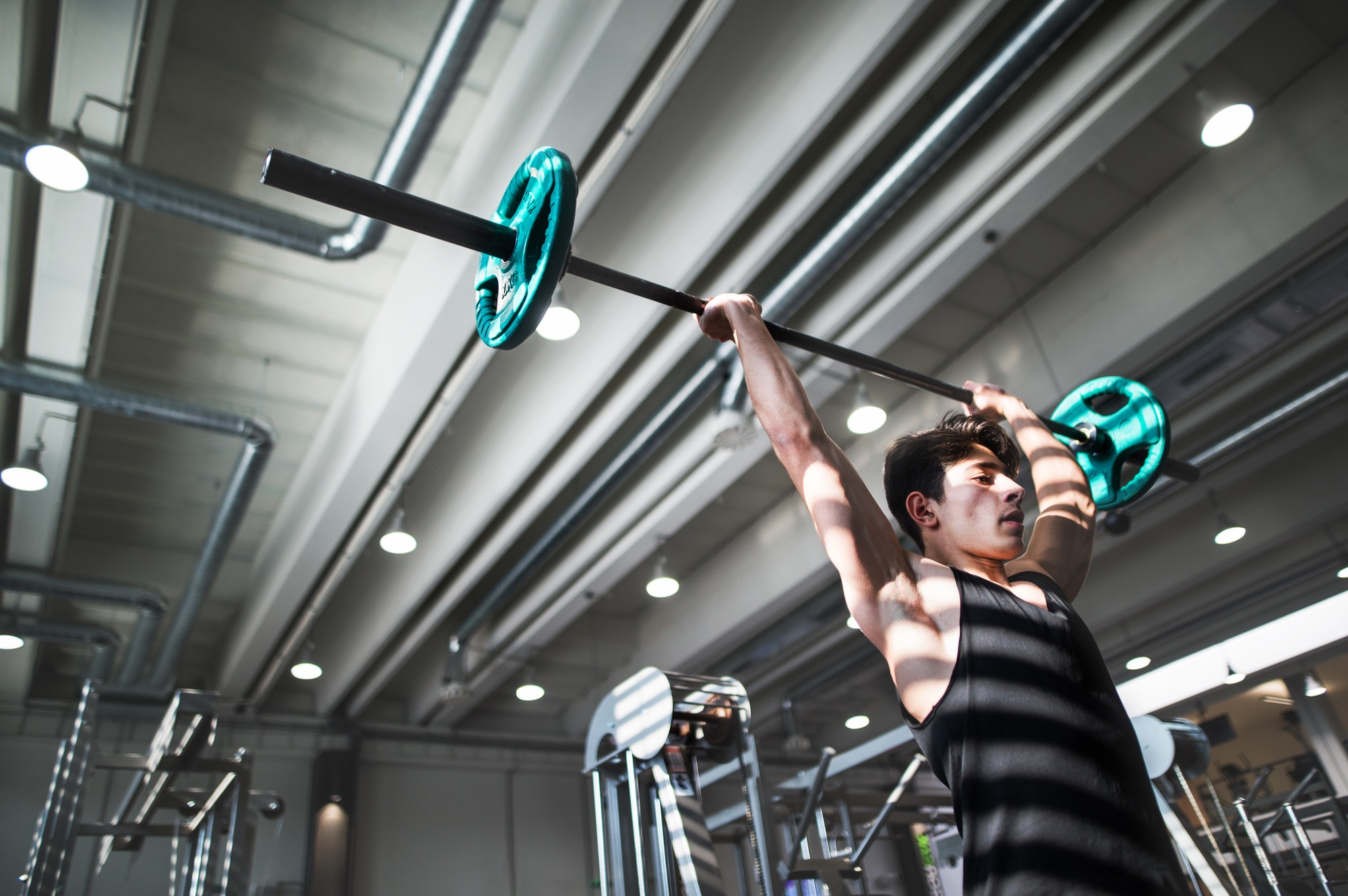 Fit young man in gym working out, lifting barbell. Copy space.
