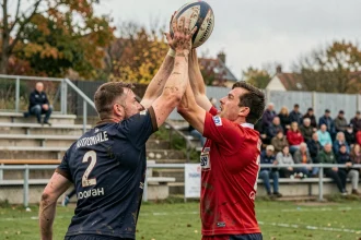 Duel en touche lors d'un match de Rugby Nationale 2 Poule 1, deux joueurs en maillots rivaux sautant pour capturer le ballon