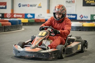 Pilote adulte en tenue de course rouge conduisant un kart dans une piste intérieure à Niort, penché dans un virage serré