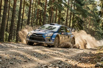 Voiture de rallye en pleine action sur une piste de gravier en forêt, championnat de rallyes 2026